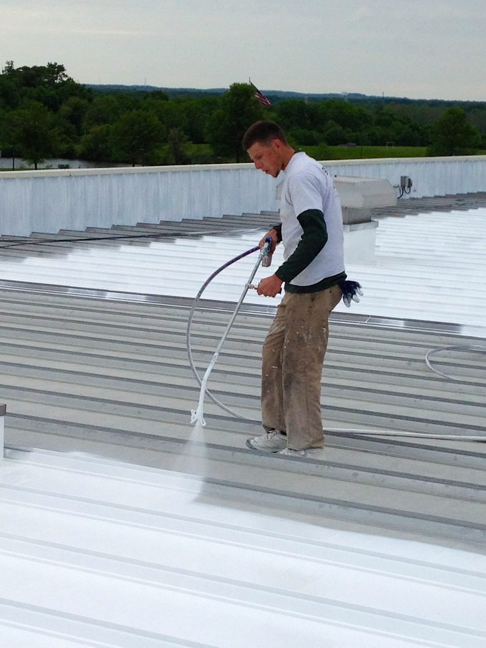 GSM technician sprayapplying white roof coating. GSM Roofing